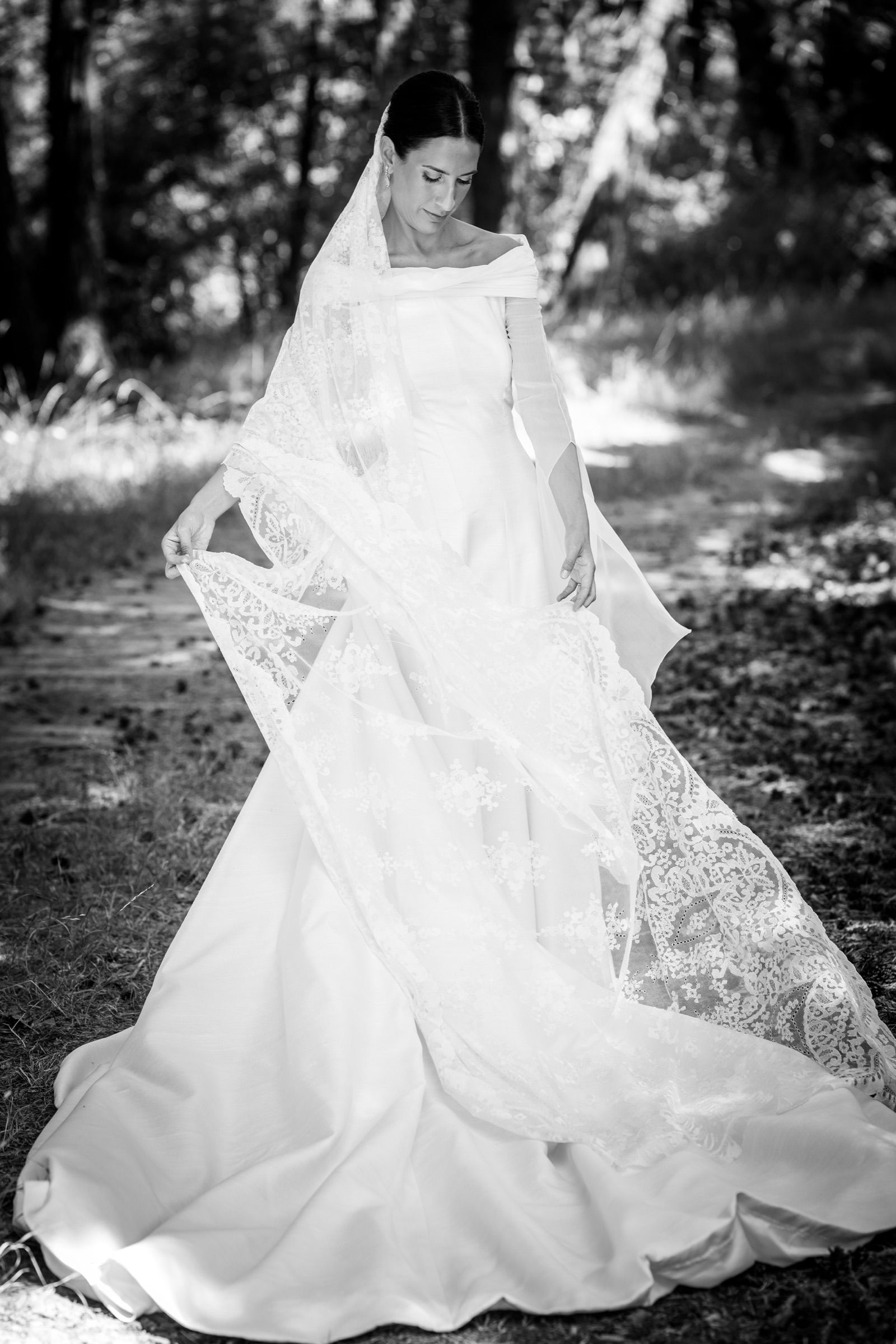 Eyes lowered, the bride fans her lace mantilla wide across her gown on a shaded path through the pines above San Juan de la Peña