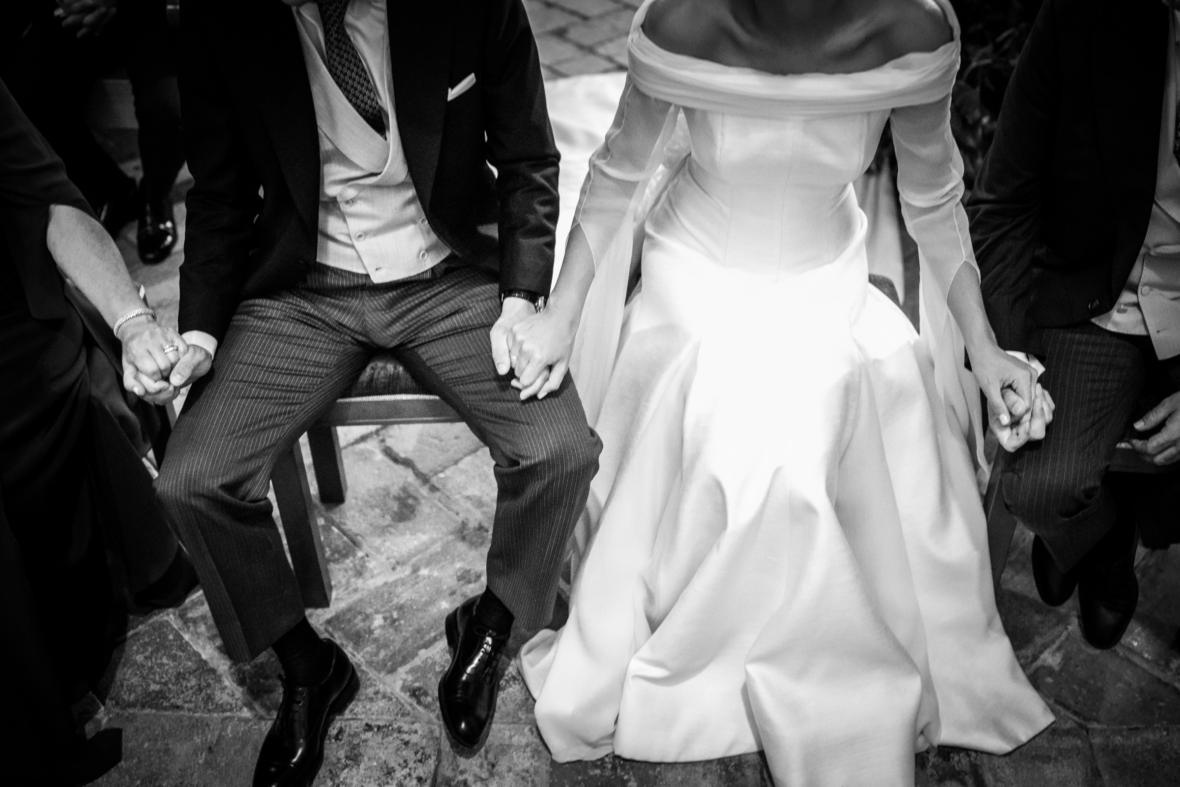 Cropped at the shoulders, the seated couple hold hands with family on either side, her satin skirt glowing against striped trousers