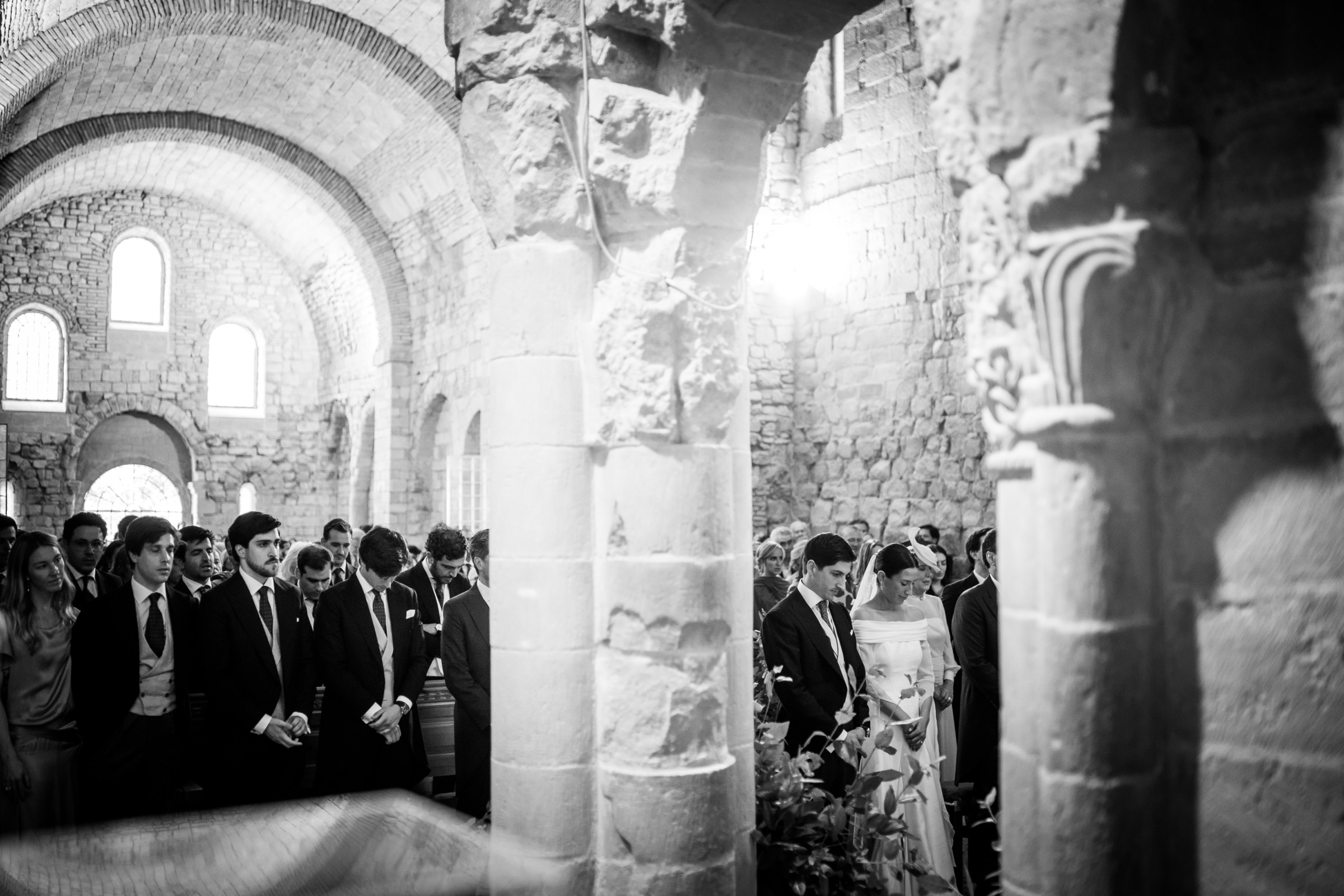 Bride and groom stand small at the altar of San Juan de la Peña, seen through the monastery's massive stone columns and layered arches