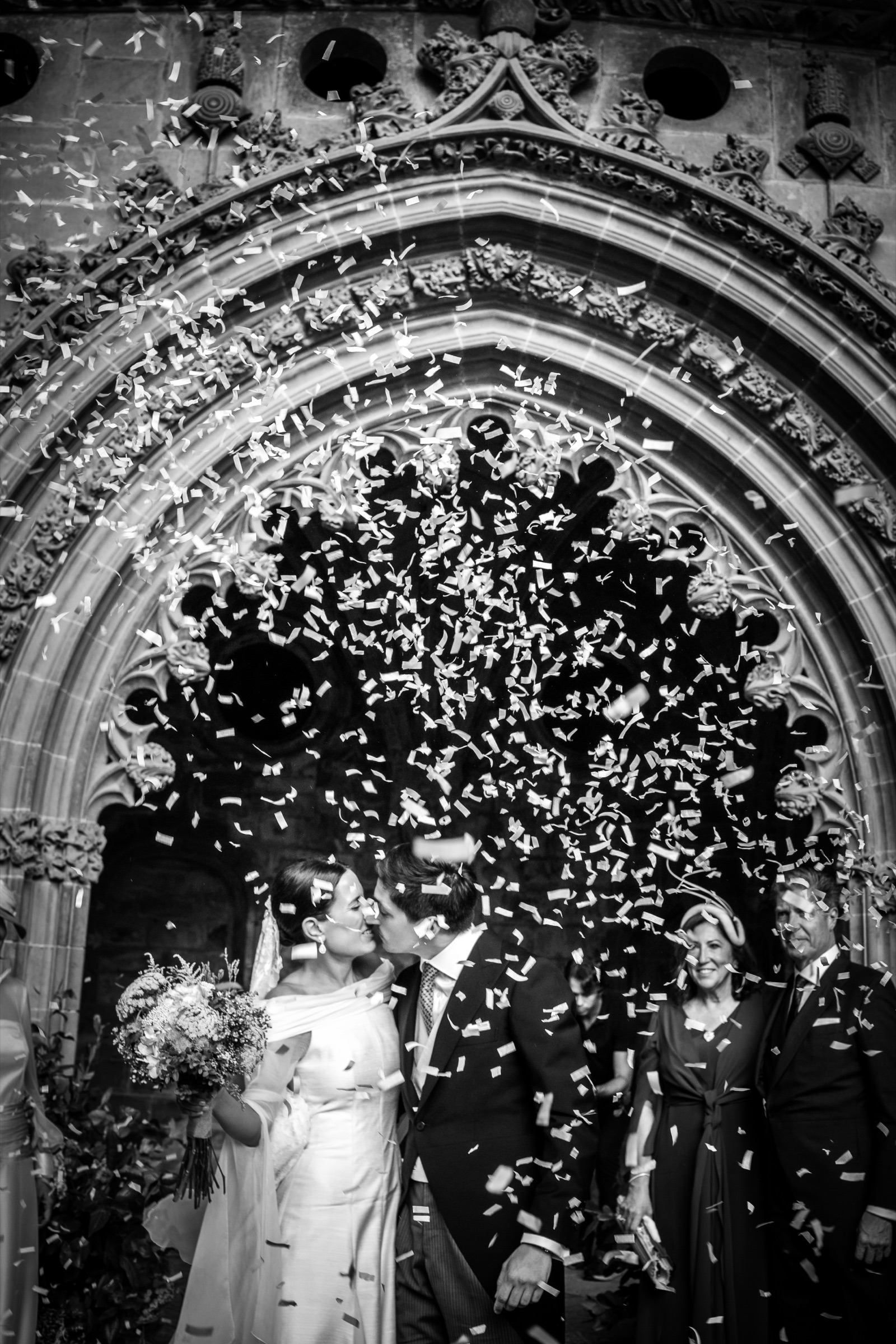 The couple kiss beneath the carved Gothic portal of San Juan de la Peña as a burst of white confetti fills the dark archway