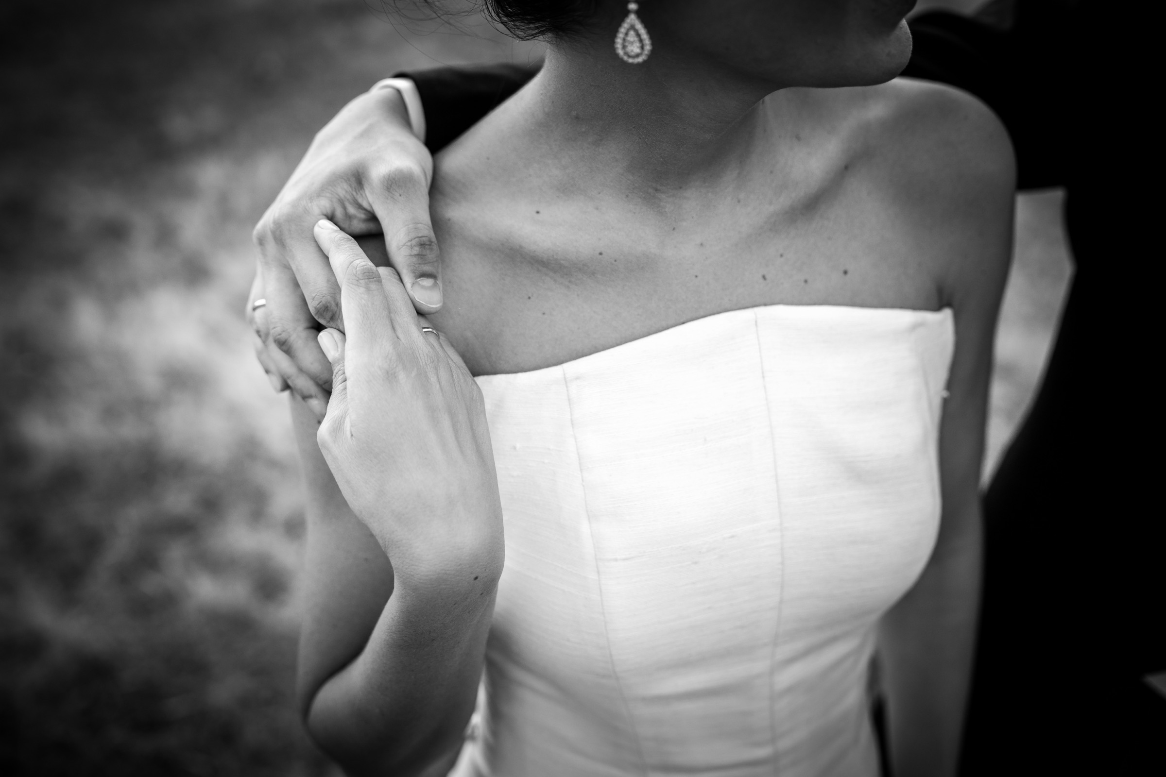The groom's hand resting on the bride's bare shoulder, her fingers reaching up to his above the seams of the bodice